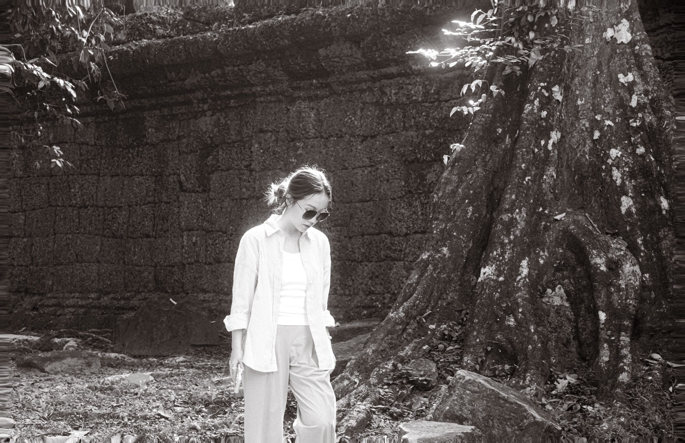 Shuhan standing beside a tree and an old stone wall